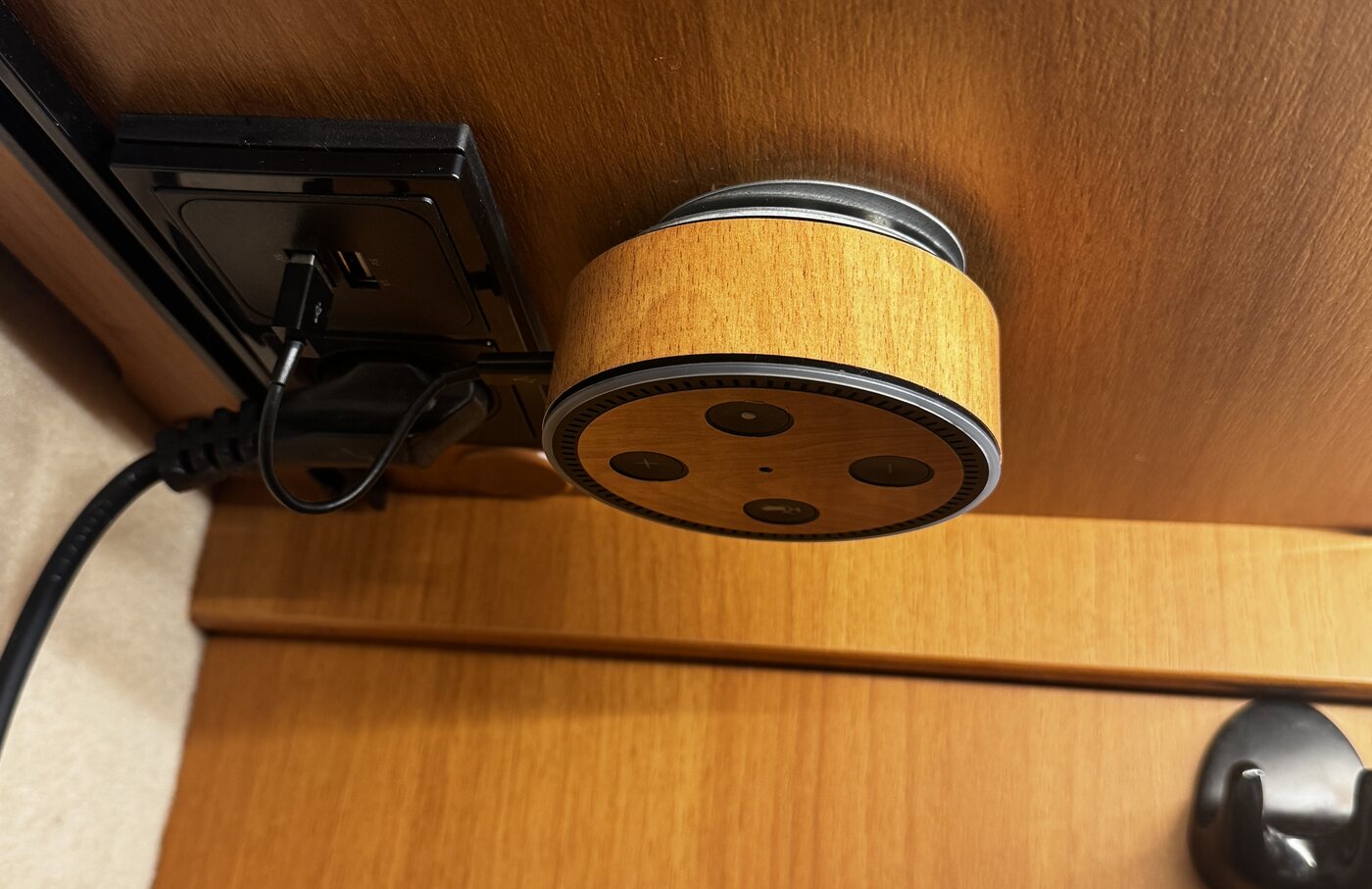 Ein kleiner Sprachassistent mit Holzfolie beklebt, unter einem Oberschrank neben einer eingebauten Steckdose mit USB-Anschluss