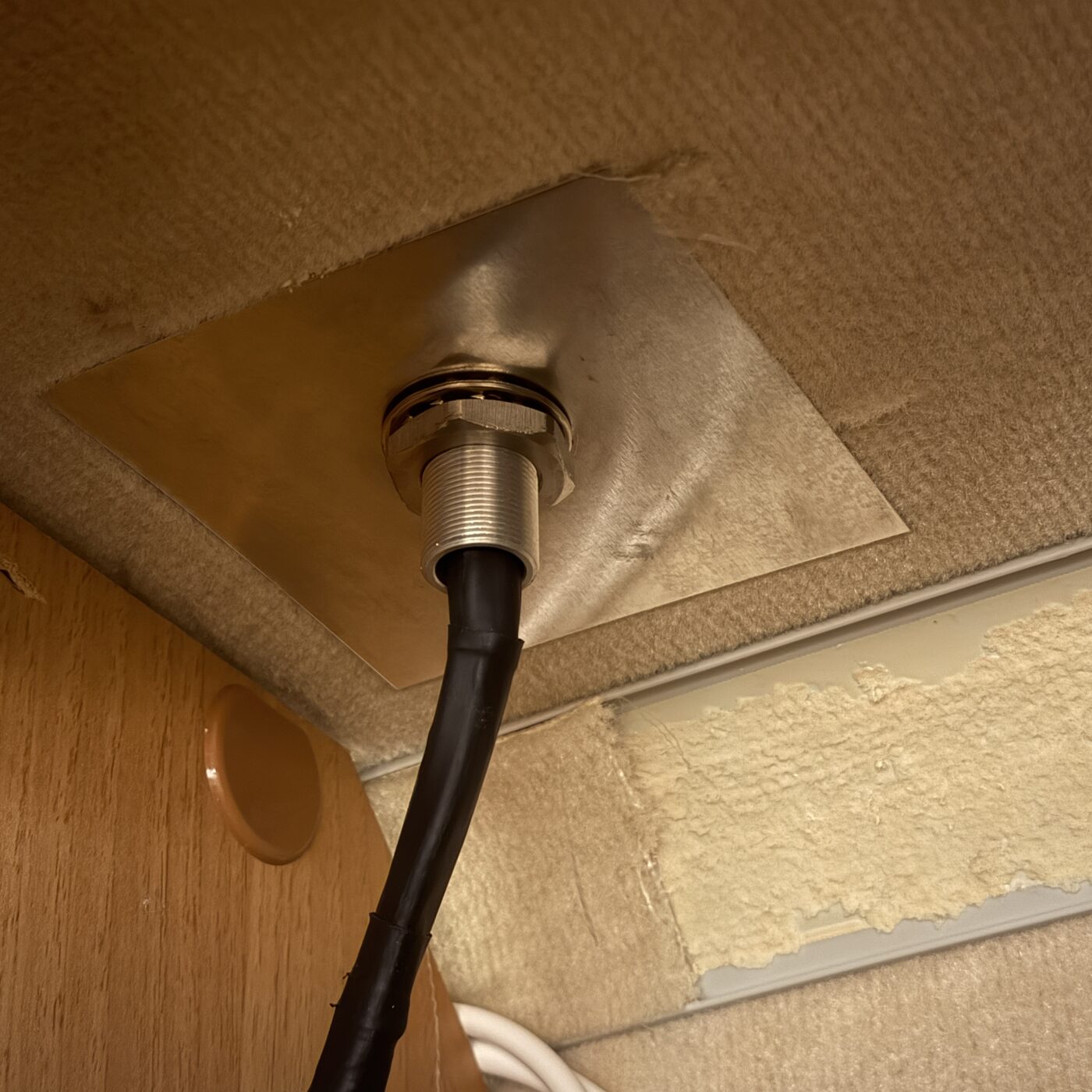 Blick von innen an die Decke, eine selbst zugeschnittene Edelstahlplatte als Gegenhalter, darin die verschraubte Gewindedurchführung der Dachantenne mit dem schwarzen Kabelbündel